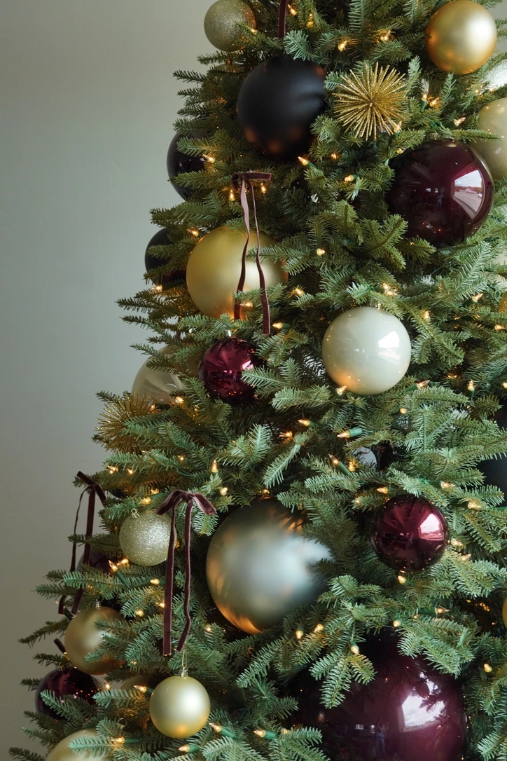 Holiday tree detail with burgundy, gold, and ivory ornaments, velvet ribbons, and warm lights